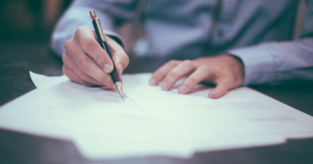 A person signing a document with a pen at a desk
